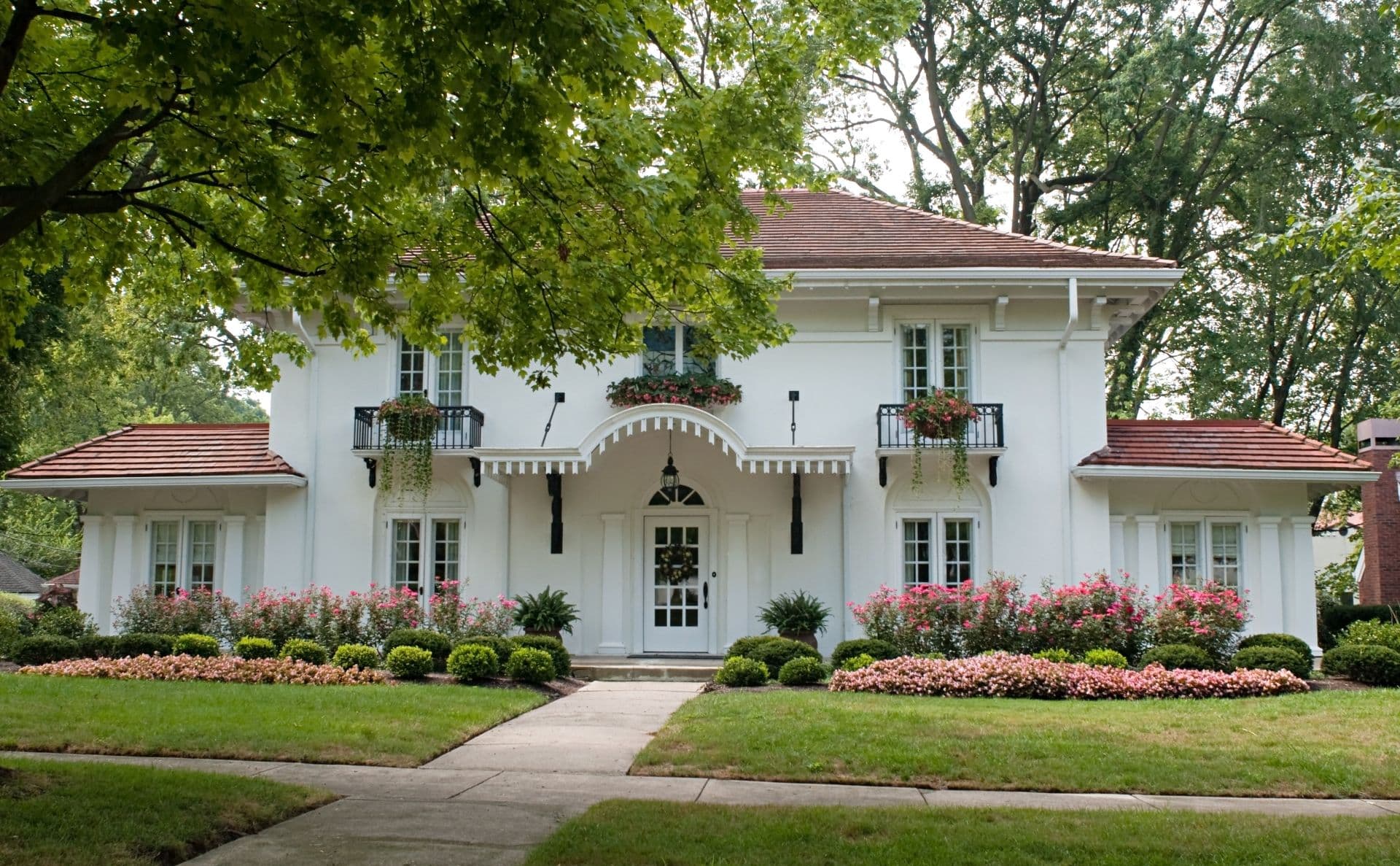 A white stucco house with red roof and pink flowers.